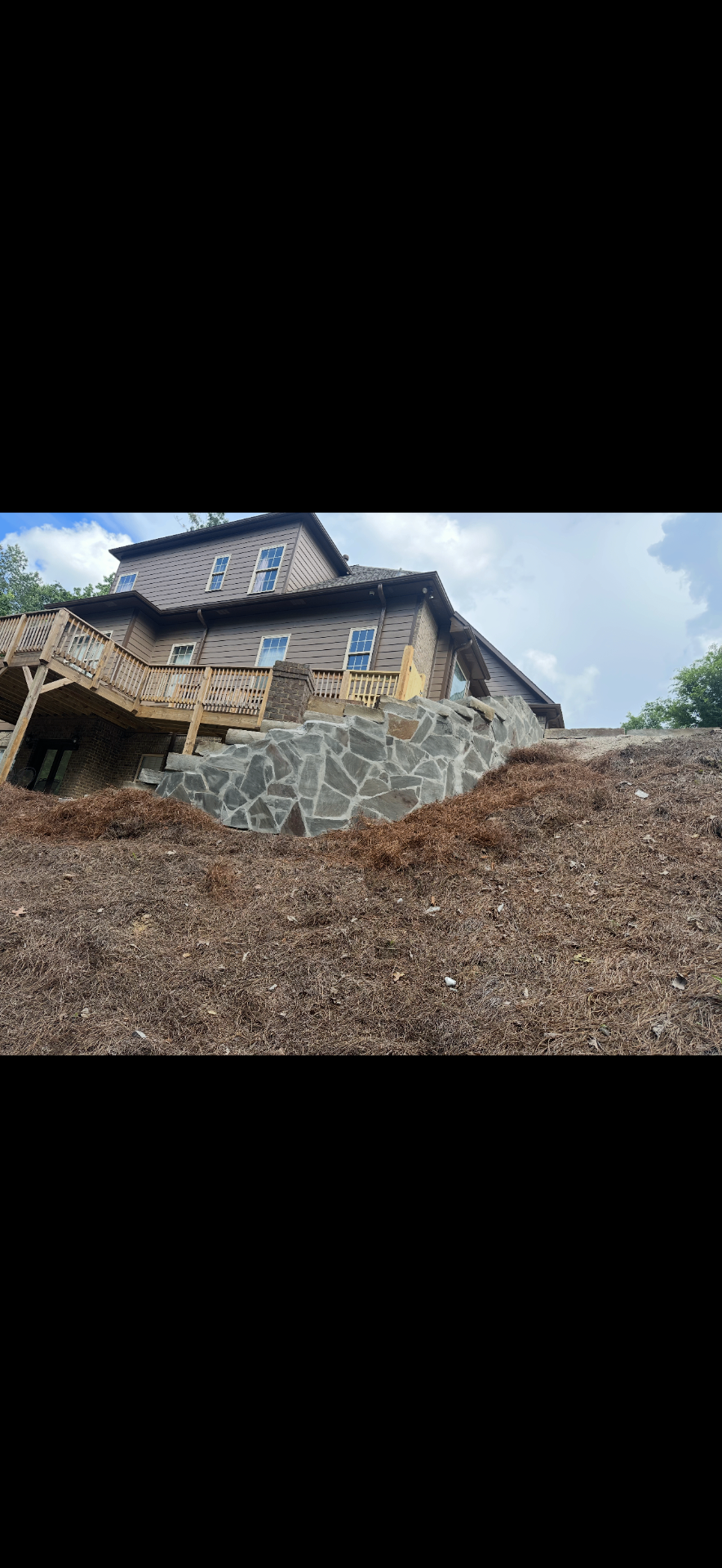 Natural stone retaining wall supporting a deck above a steep slope